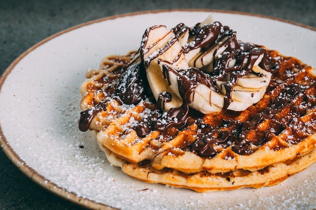 Gros plan de crêpes au chocolat et aux bananes servies sur une assiette blanche