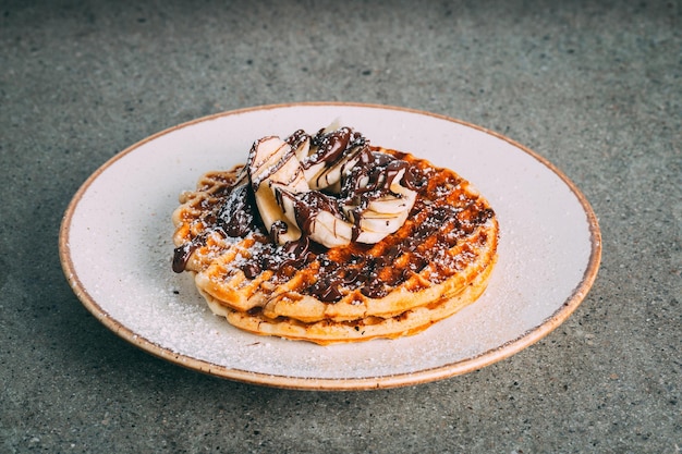 Gros plan de crêpes au chocolat et aux bananes servies sur une assiette blanche