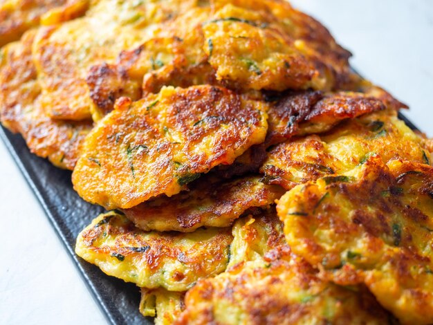 Gros plan sur des crêpes à base de courgettes et de légumes disposés sur une assiette sombre. Un délicieux plat végétarien. Vue de côté