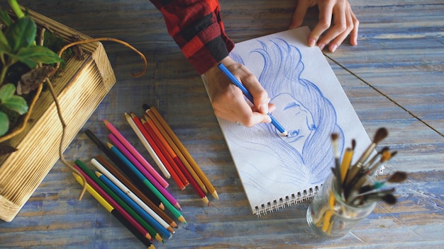 Gros plan d'un croquis de peinture à la main féminine sur un cahier en papier avec des crayons