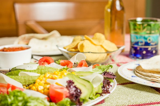 Gros plan de la cuisine mexicaine traditionnelle dans une table, avec une assiette de salade fraîche, des tortillas, des fajitas au poulet, des nachos et un bol de sauce épicée