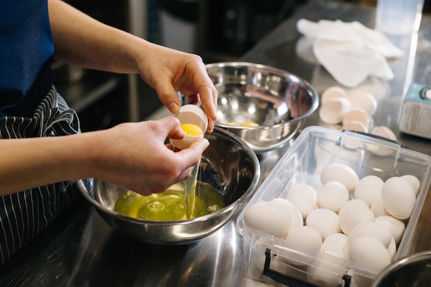 Gros plan Un cuisinier dans la cuisine d'un café ou d'une boulangerie Des mains féminines cassent des œufs pour la pâte