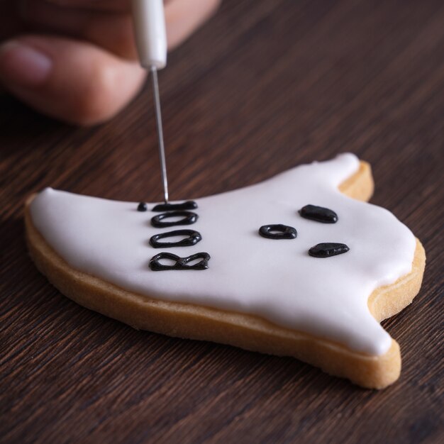 Gros plan de la décoration de mignons biscuits de pain d'épice fantôme Halloween avec sac de garniture de crème glacée glaçage.