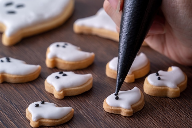 Gros plan de la décoration de mignons biscuits de pain d'épice fantôme Halloween avec sac de garniture de crème glacée glaçage.