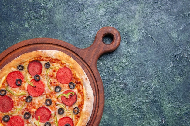 Gros plan d'une délicieuse pizza sur une planche à découper en bois sur le côté droit sur une surface bleu foncé avec un espace libre