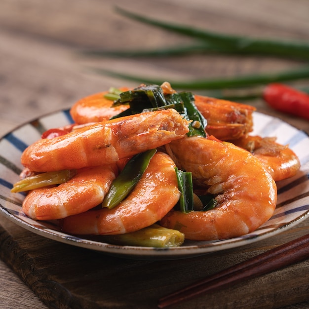 Gros plan de délicieuses crevettes poêlées maison dans une assiette sur une surface de table en bois sombre.