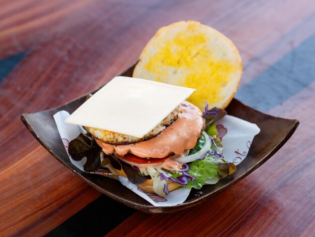 Gros plan d'un délicieux délicieux petit-déjeuner maison délicieux cheeseburger de boeuf grillé avec de la laitue de légumes en tranches, du chou, de l'oignon et de la sauce épicée fondante dans un bol en bois sur une table en bois