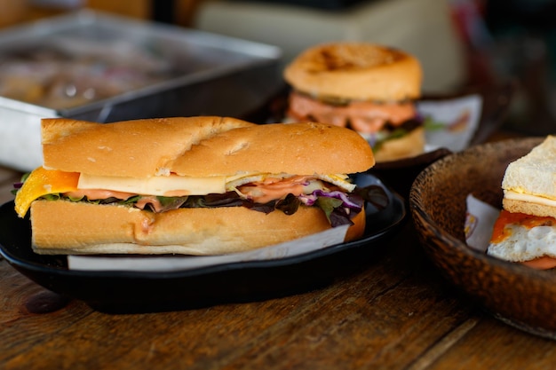 Gros plan d'un délicieux délicieux sandwich à la dinde à pain long fait maison avec de la saucisse au fromage coupée en tranches de légumes tomate chou laitue dans un bol en bois sur une table en bois