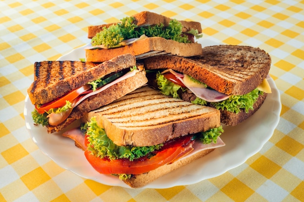 Gros plan de délicieux sandwichs au jambon, tomates, fromage et herbes sur une assiette sur la table