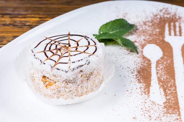 Gros plan sur un dessert décadent avec une conception de toile d'araignée sur une plaque blanche avec une garniture de feuilles de menthe et des contours d'ustensiles saupoudrés de copeaux de chocolat