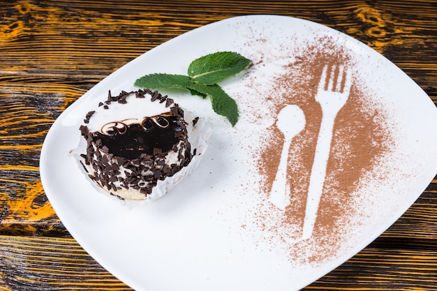 Gros plan sur un dessert décadent enrobé de copeaux de chocolat et servi sur une assiette avec une garniture de feuilles de menthe et des contours d'ustensiles saupoudrés de cacao et reposant sur une surface de table en bois