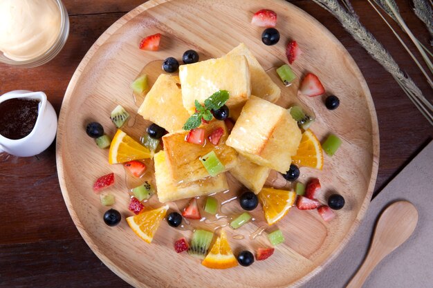 Gros plan de dessert qui contient du pain, des baies aux fraises, des myrtilles, du kiwi, de l&#39;orange pour le caramel et met la feuille de menthe poivrée sur le dessus du bois et sur la table en bois