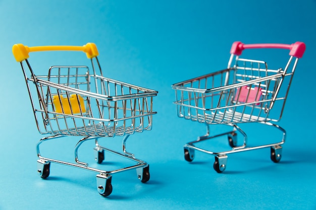 Gros plan sur deux chariots d'épicerie de supermarché pour faire du shopping avec des roues et des éléments en plastique jaune et rose sur la poignée isolés sur fond bleu. Concept de shopping. Copiez l'espace pour la publicité.