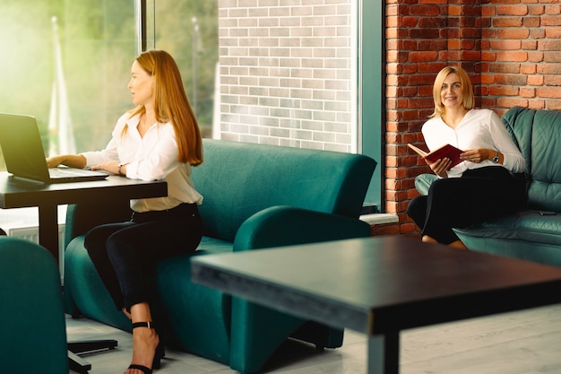 Gros plan de deux femme d'affaires à l'aide d'un ordinateur portable et lire le livre en pause de travail. Concept commercial et financier. Concept de personnes et de modes de vie. Conception de bureau moderne sur le lieu de travail.