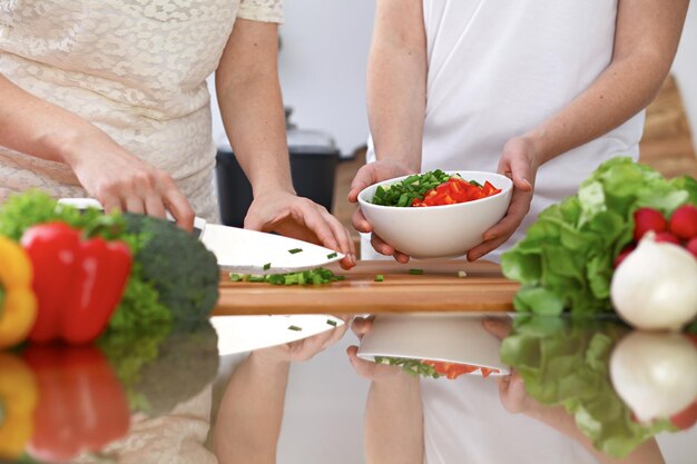 Gros plan de deux femmes cuisinent dans une cuisine. Amis s'amusant en préparant une salade fraîche.