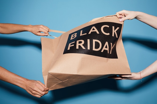 Gros plan de deux femmes tirant le sac en papier du Black Friday sur le fond bleu