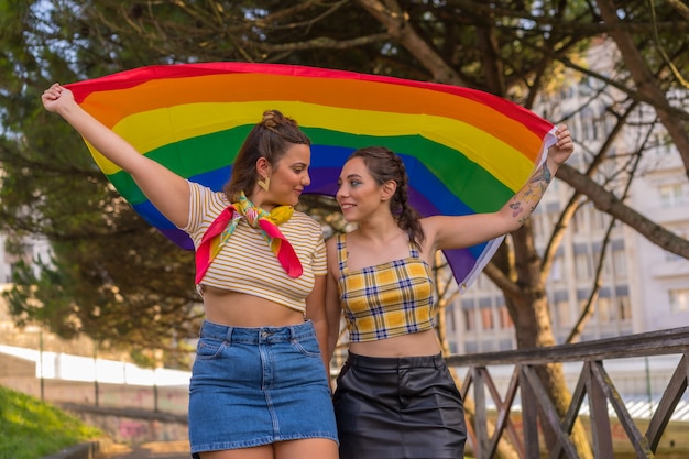 Un gros plan sur deux jeunes femmes de race blanche tenant un drapeau de fierté LGBT à l'extérieur