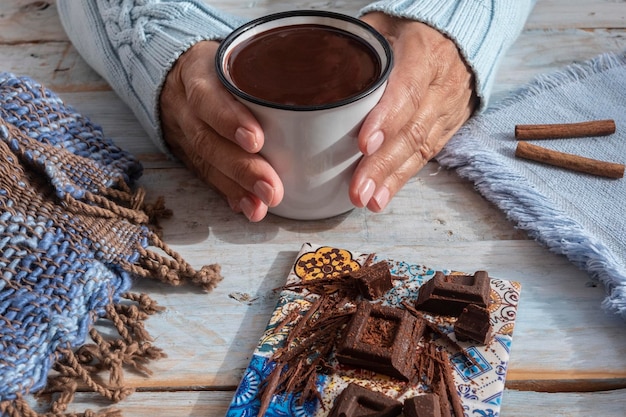 Gros plan de deux mains humaines féminines tenant une tasse de chocolat noir crémeux et épais Table en bois comme arrière-plan et écharpe