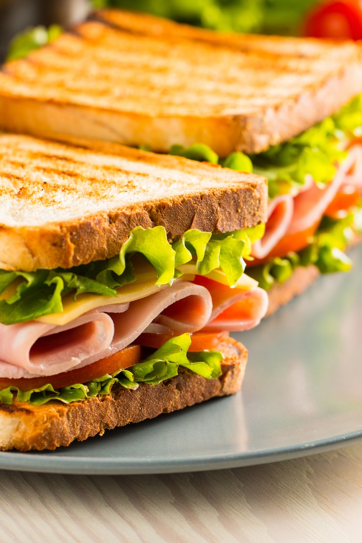 Photo gros plan de deux sandwichs au bacon, salami, prosciutto et légumes frais sur une planche à découper en bois rustique. concept de sandwich au club.