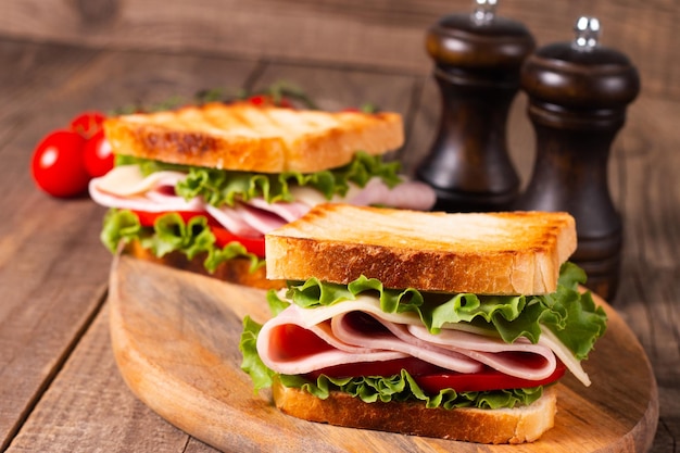 Gros plan de deux sandwichs grillés avec du jambon frais, du fromage et des légumes en arrière-plan.