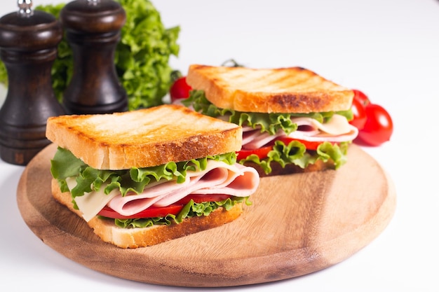 Gros plan de deux sandwichs grillés avec du jambon frais, du fromage et des légumes en arrière-plan.