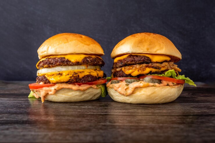 Un gros plan de deux sandwichs de hamburger au bacon avec frites, laitue, fromage fondu, oignons sucrés et tomate double patty sur une table en bois