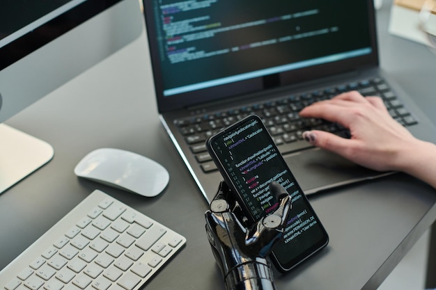 Gros plan sur un développeur tapant des codes de sécurité sur un smartphone et un ordinateur portable pour un nouveau programme informatique