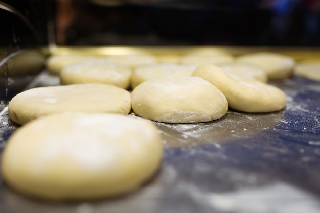 Gros plan sur différents types de pâte à pizza saupoudrée de farine de blé blanc cuisant dans le grill dans un camion de nourriture dans la rue.