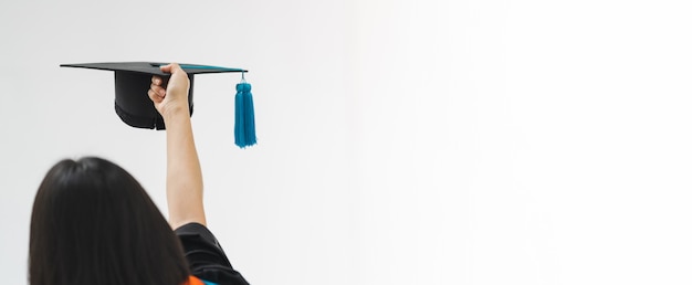 Gros plan d'un diplômé universitaire en robe de graduation titulaire d'un diplôme avec mortier pour montrer et célébrer le succès le jour de la rentrée universitaire. Éducation stock photo