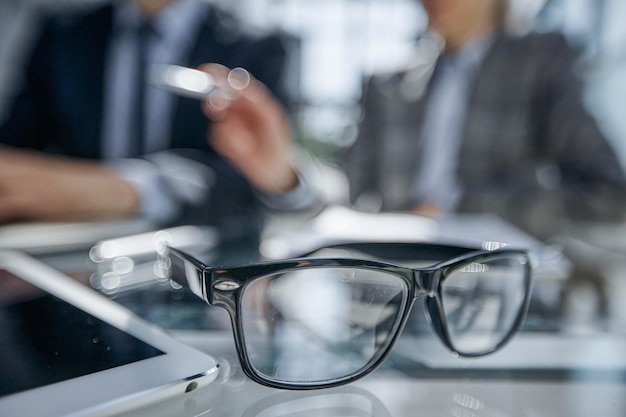 Gros plan de documents commerciaux posés sur une table de réunion, silhouettes floues d'employés masculins vues en arrière-plan