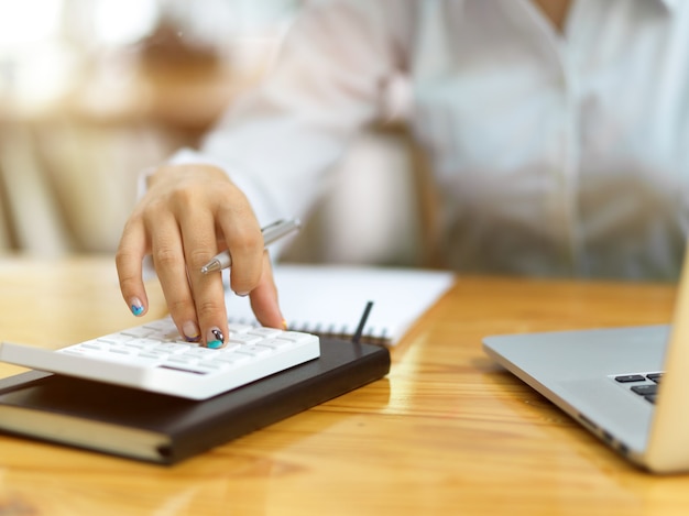 Gros plan sur les doigts des femmes d'affaires à l'aide de la calculatrice au bureau, comptable calculant le bénéfice net