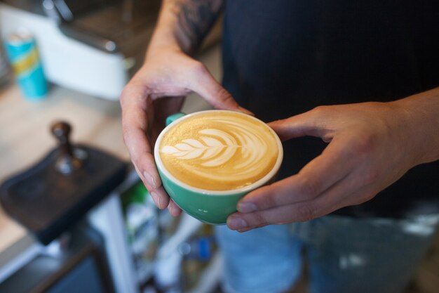 Gros plan du barista tenant un cappuccino aromatique. Café prêt à vendre. Mains mâles tenant une tasse de café.