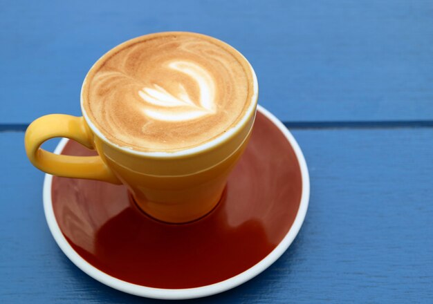 Gros plan du café cappuccino dans une tasse brun jaune isolé sur une table en bois bleu