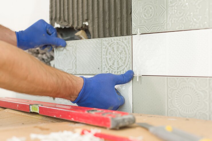 Gros plan du carreleur posant des carreaux de céramique sur le mur dans la cuisine, rénovation