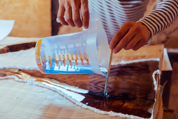 Gros plan du charpentier versant de l'époxy liquide dans une table en bois