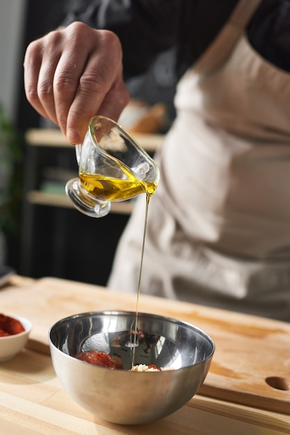 Gros plan du chef ajoutant de l'huile dans le bol avec de la salade il fait un plat spécial