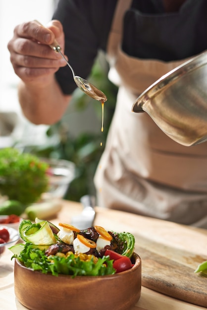 Gros plan du chef ajoutant de la sauce soja dans un plat avec de la viande et des légumes à la table