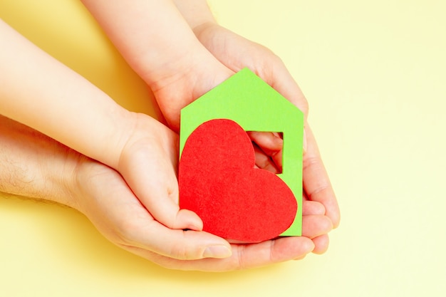 Gros plan du coeur rouge en papier et coeur rouge dans les mains de l'enfant et du papa sur fond jaune. Concept de logement familial.