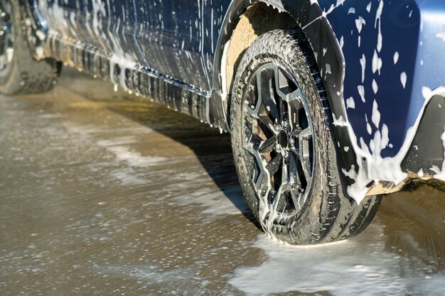 Gros plan du conducteur masculin lavant sa voiture avec un jet d'eau haute pression sans contact dans un lave-auto en libre-service.