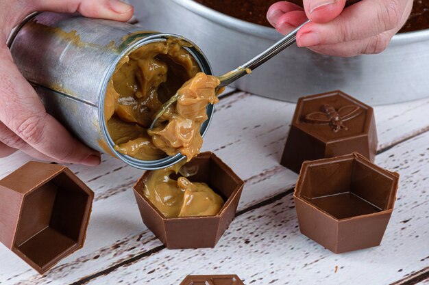 Gros plan du confiseur mettant une cuillère de dulce de leche dans de petits moules à chocolat pour faire un gâteau au miel brésilien.