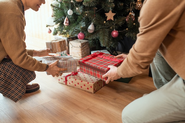 Gros plan du couple assis sur le sol et empiler des cadeaux de Noël sous l'arbre