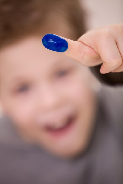 Photo gros plan du doigt du garçon dans la peinture bleue. dessin de garçon enfant souriant. activités enfants. mise au point sélectionnée