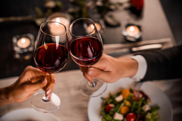 Gros plan du jeune couple grillage avec des verres de vin rouge au restaurant