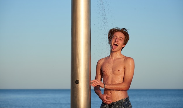Un gros plan du jeune homme buvant de l'eau d'une douche sur la plage.