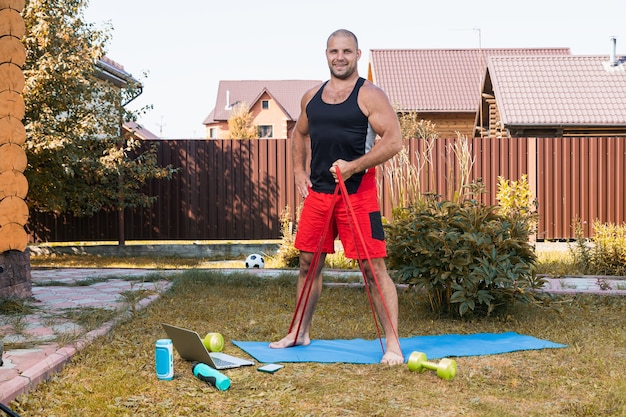 Gros plan du jeune homme fait du sport à la maison dans l'arrière-cour en été. Jeune sportif faisant de l'exercice avec du caoutchouc sport