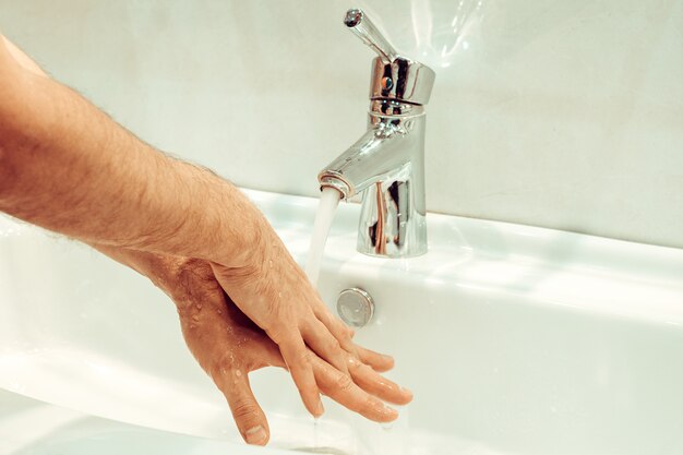 Gros plan du jeune homme de race blanche se laver les mains avec du savon dans l'évier de la salle de bain Hygiène personnelle