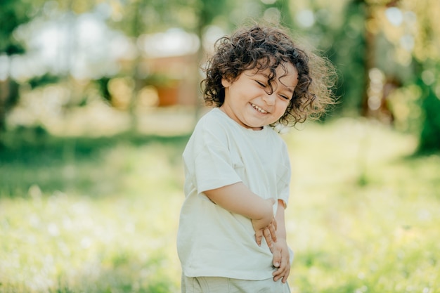 Gros plan du joyeux petit garçon aux cheveux bouclés riant dans le jardin vert frais