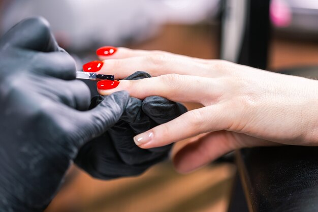 Gros plan du maître en gants en caoutchouc couvrant les ongles rouges avec top coat dans le salon de beauté