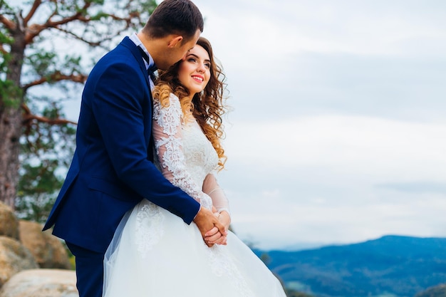 Gros plan du marié embrasse la mariée de l'arrière sur les rochers avec une vue magnifique