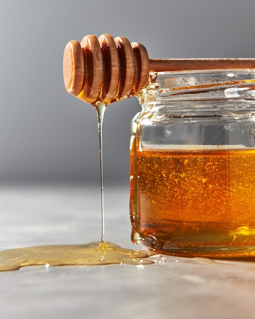 Gros plan du miel de fleur douce naturelle dégoulinant de bâton sur une table en pierre grise rosh hashanah juif